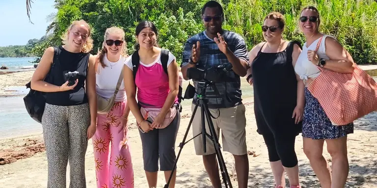 A group of travelers on the beach with their guide and his spotting scope